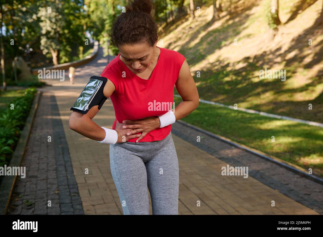 Determined middle aged fit woman, runner, sportswoman holds her stomach