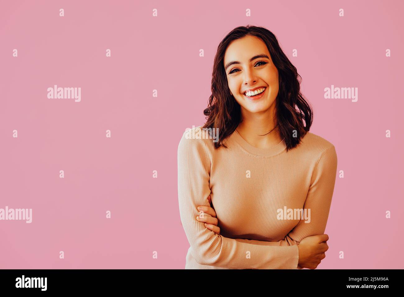 Young brunette woman smiling girl posing isolated on pink background studio portrait. People sincere emotions lifestyle concept. Holding hands crossed. positive Stock Photo