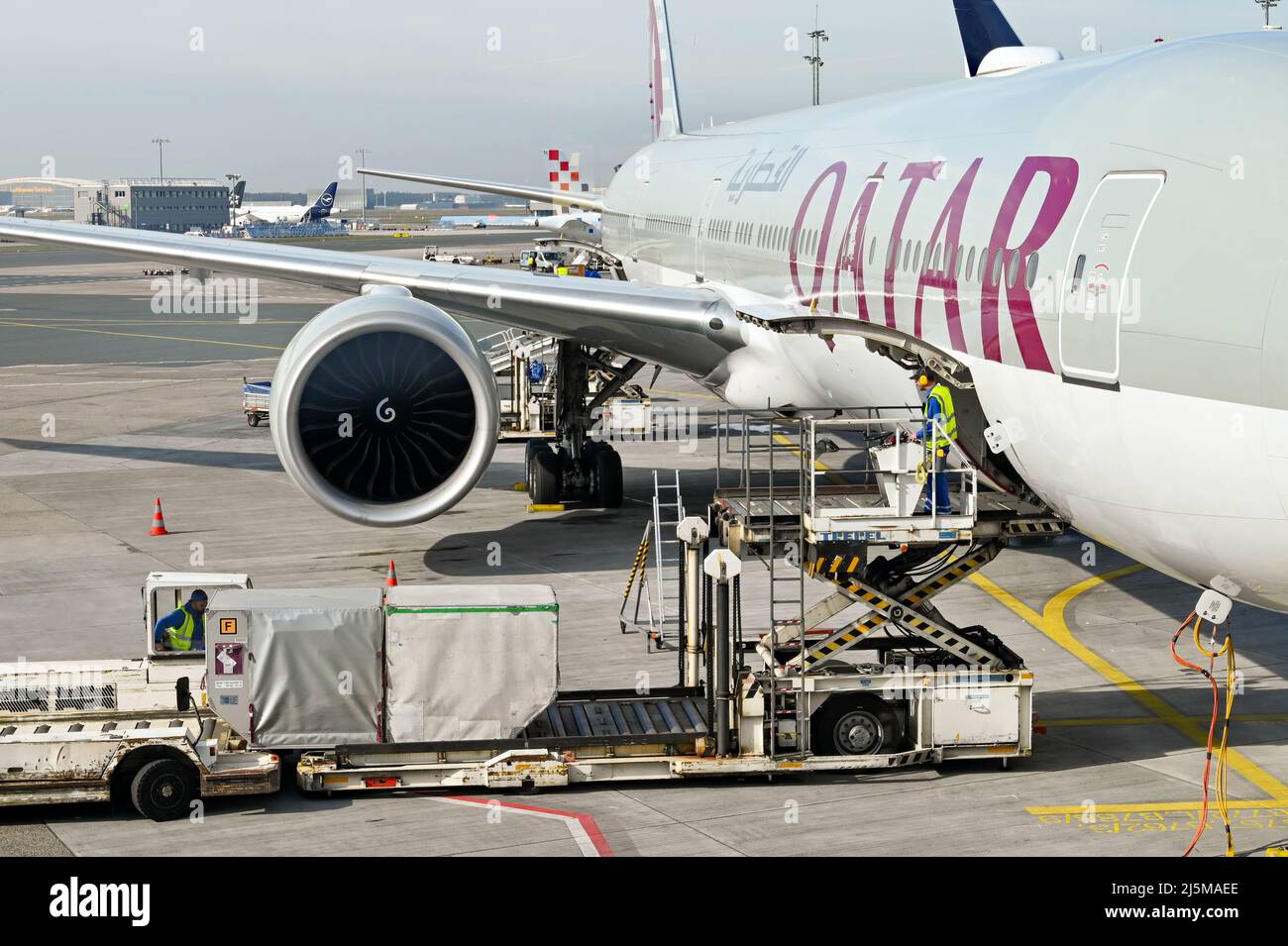 Frankfurt, Germany - April 2022: Airport worker operating an air freight pallet loader to load containers into the cargo hold of a Qatar Airways jet Stock Photo