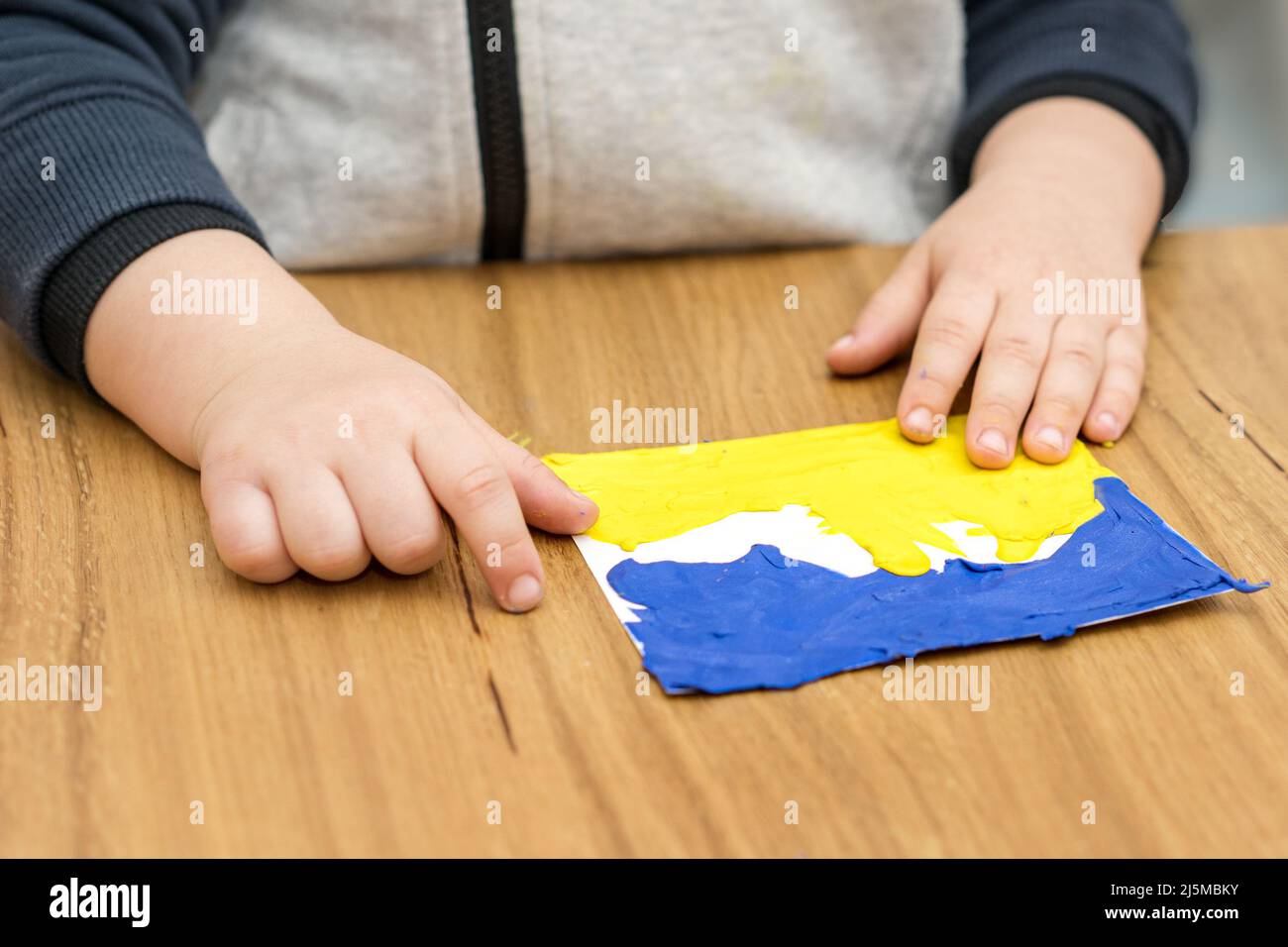Close up child hands sculpts from colored plasticine Ukraine flag. Stock Photo