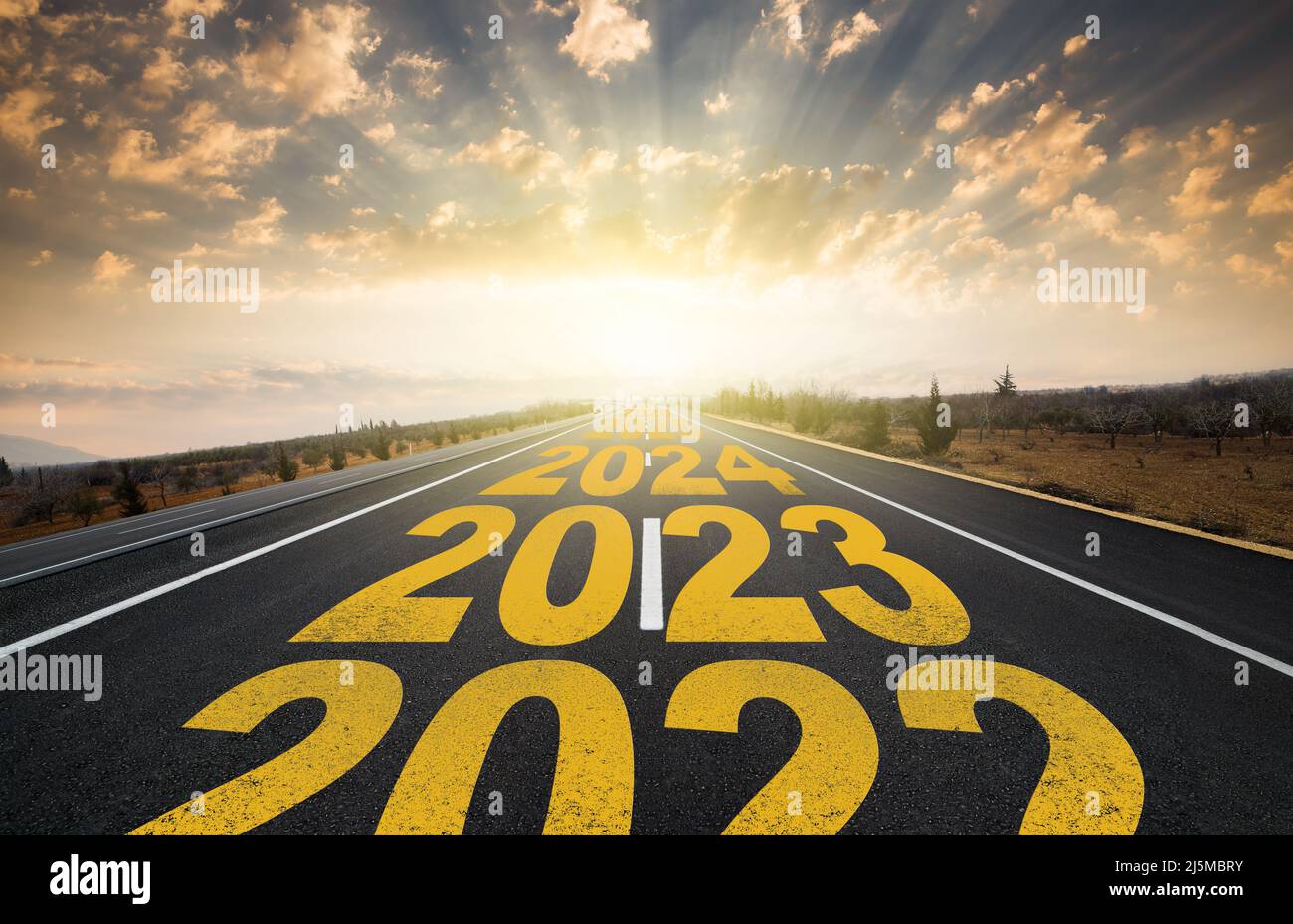 The word 2023 written on highway road in the middle of empty asphalt road at golden sunrise. New year 2023 concept. Concept of planning and challenge Stock Photo