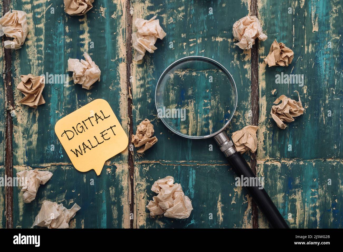 DIGITAL WALLET text on a sticky note on a green wooden background, crumpled notes and a magnifying glass lie nearby Stock Photo