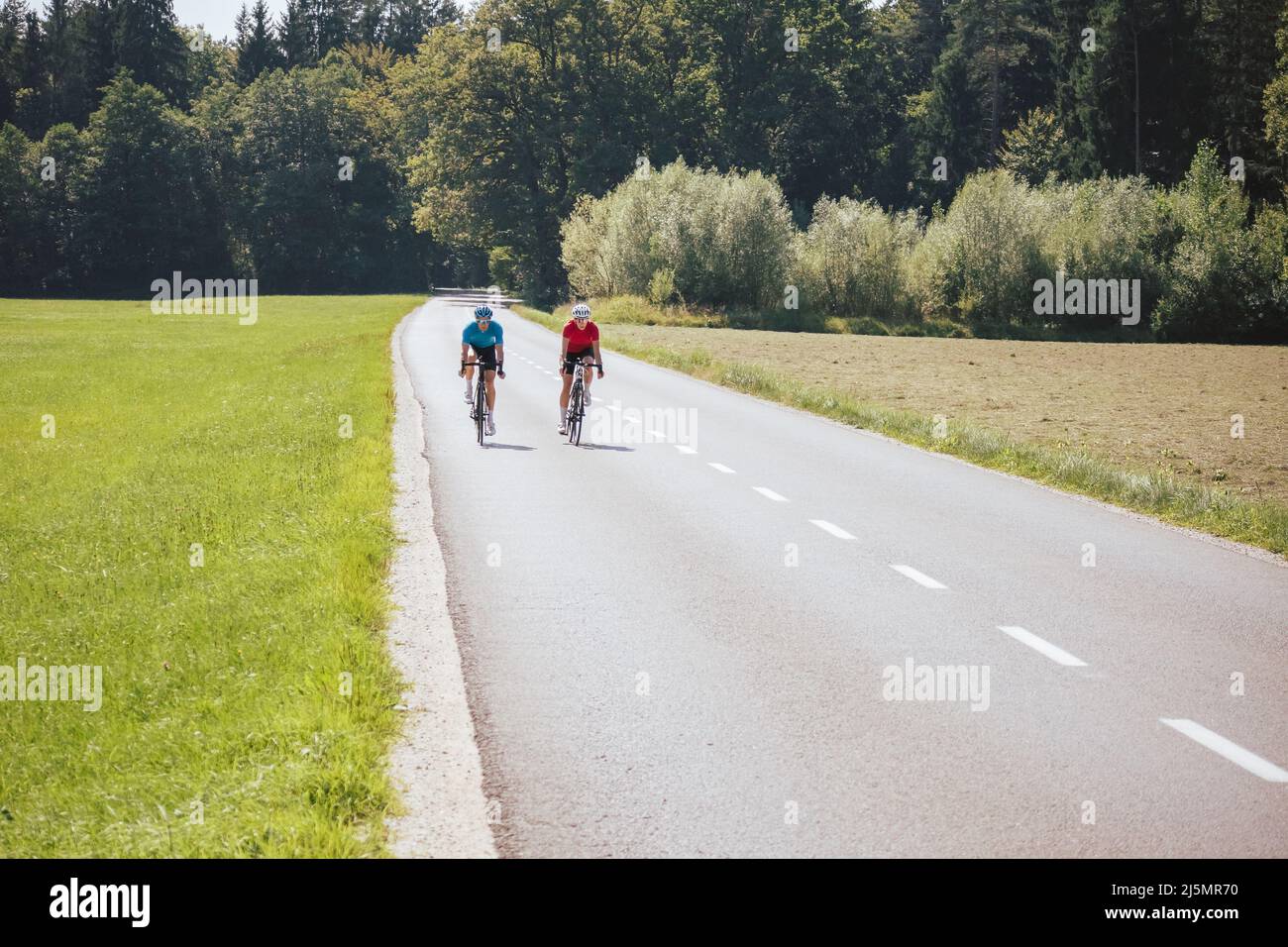 Cyclists couple on the road in summer cycling gear pedaling and gliding positions on racing cycles. Stock Photo
