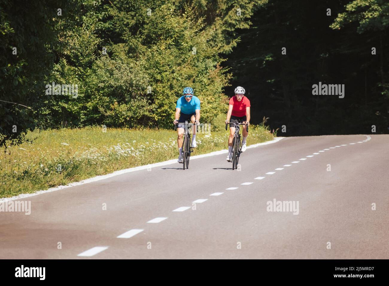 Cyclists couple on the road in summer cycling gear pedaling and gliding positions on racing cycles. Stock Photo