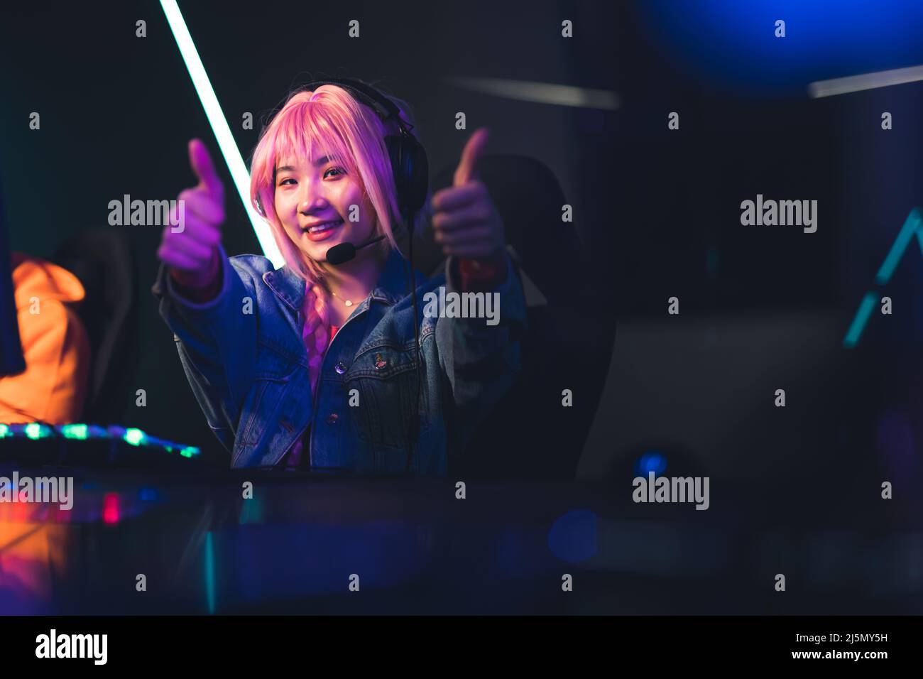 Young Asian female player showing thumbs up dark background copy space video games concept . High quality photo Stock Photo