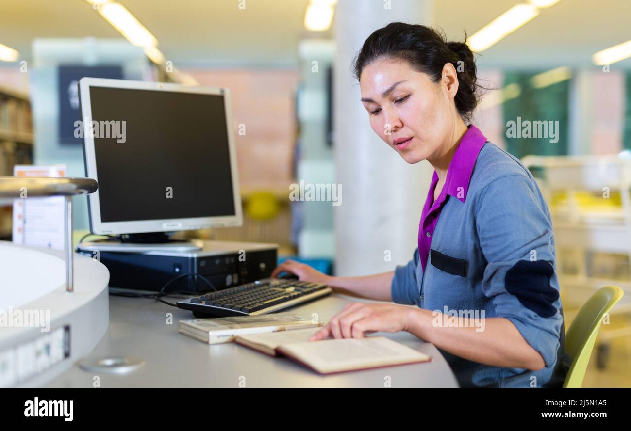 Asian student girl is working with a book while sitting in front of a computer Stock Photo