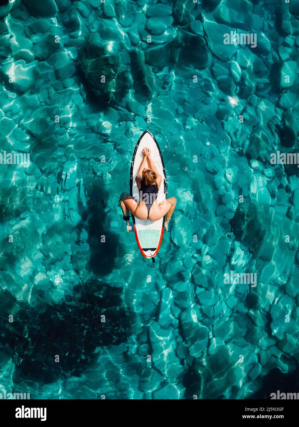 Surf girl on surfboard and wait wave in transparent ocean. Aerial view