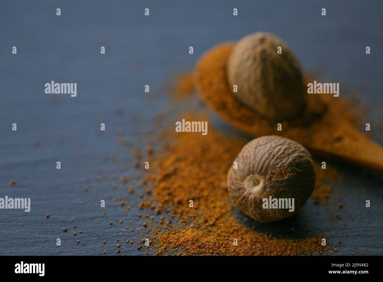 Nutmeg and nutmeg powder in a spoon on a black slate background.Spices and condiments.Nutmeg close-up on a dark background. Dark mood. Stock Photo
