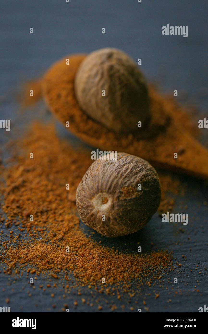 Nutmeg and nutmeg powder in a spoon on a black slate background.Nutmeg close-up on a dark background. Dark mood. Stock Photo