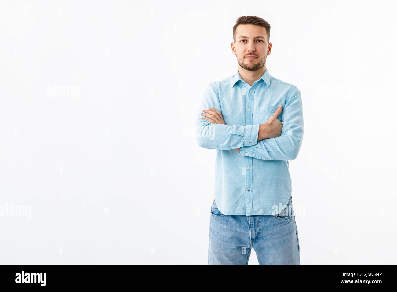 Portrait of a cheerful young man in a blue shirt on a white background. The guy stands, looks at the camera and smiles. Stock Photo