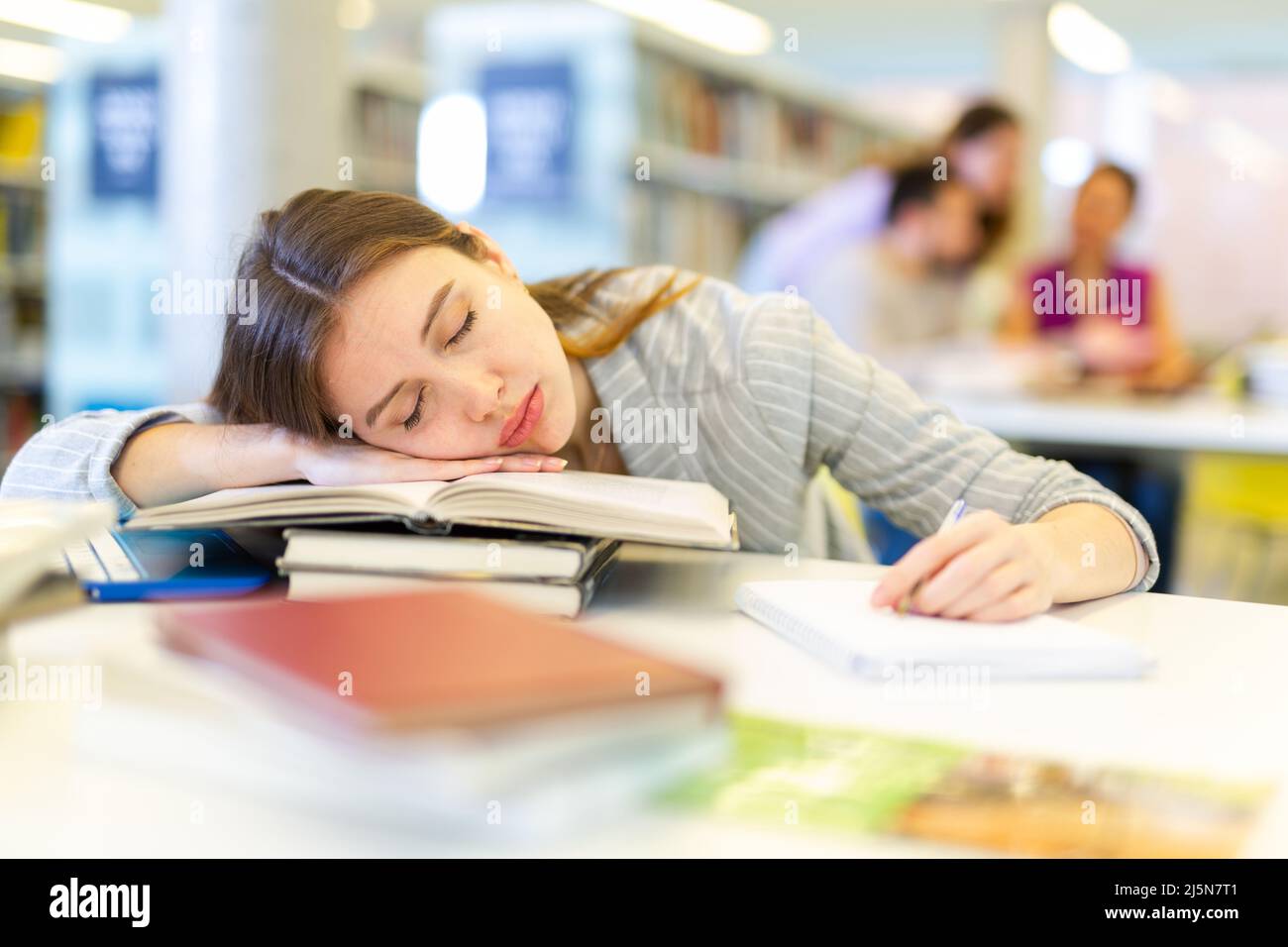 Tired female student sleeping on stack of books in library Stock Photo