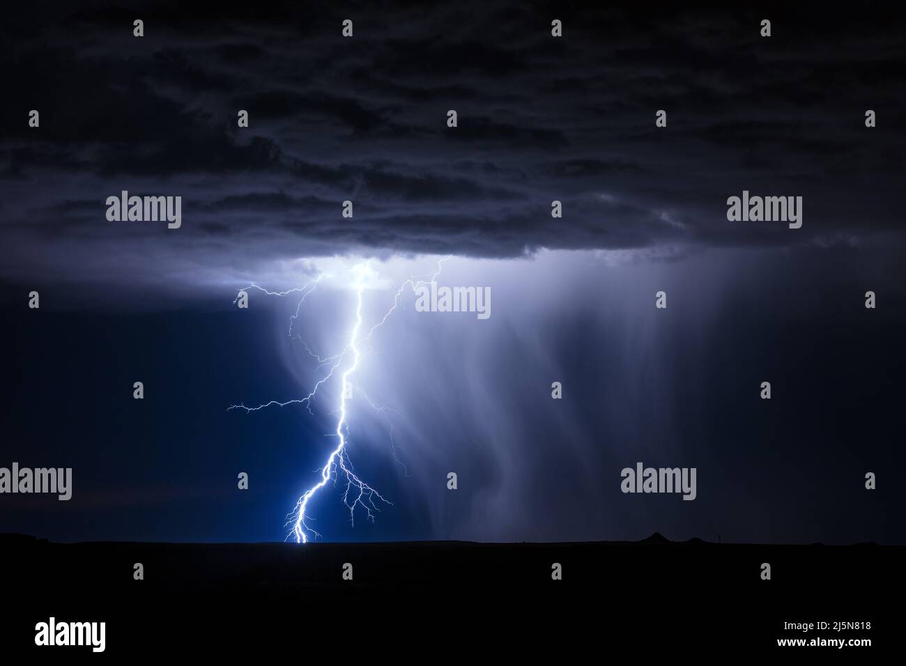 A lightning bolt illuminates rain falling from a thunderstorm near Holbrook, Arizona Stock Photo