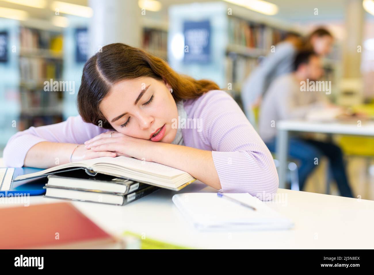 Tired female student sleeping on stack of books in library Stock Photo ...