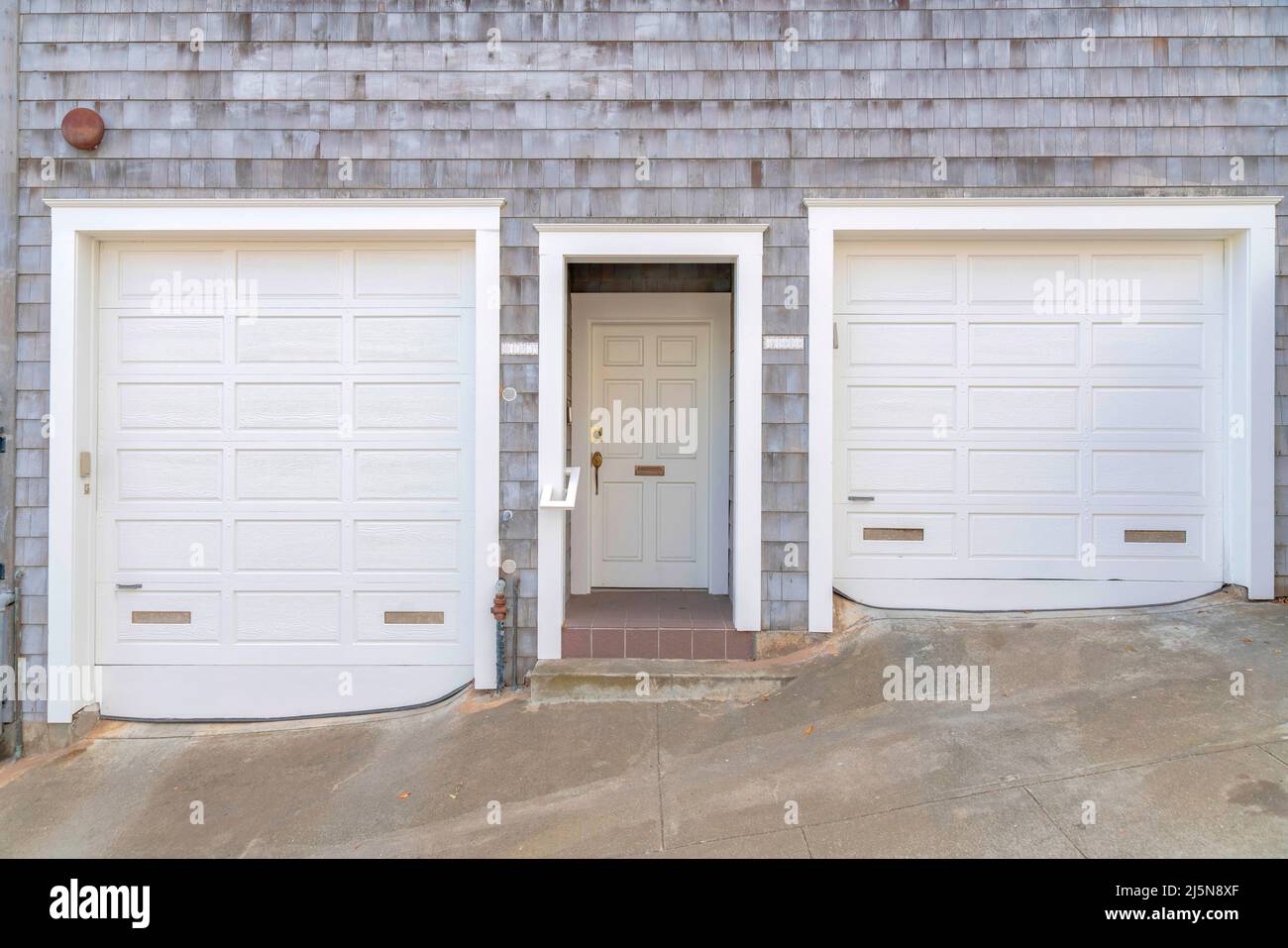 Facade of a house on a concrete slope with two white garage doors at San  Francisco, California. Home exterior with gray shingles wall cladding and  whi Stock Photo - Alamy