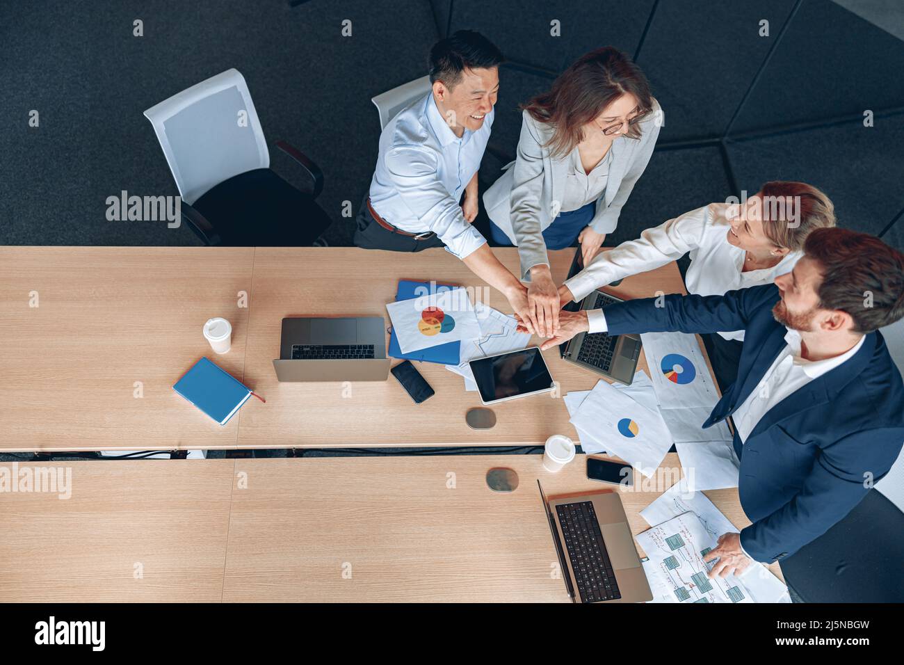 Diverse business people group put hands together while standing near the table in office Stock Photo