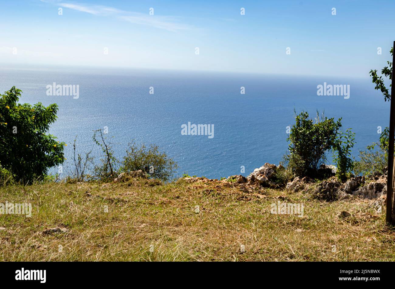 Low grass covers the landscape leading to the rocky edge bordering the sea that meets the sky. Stock Photo