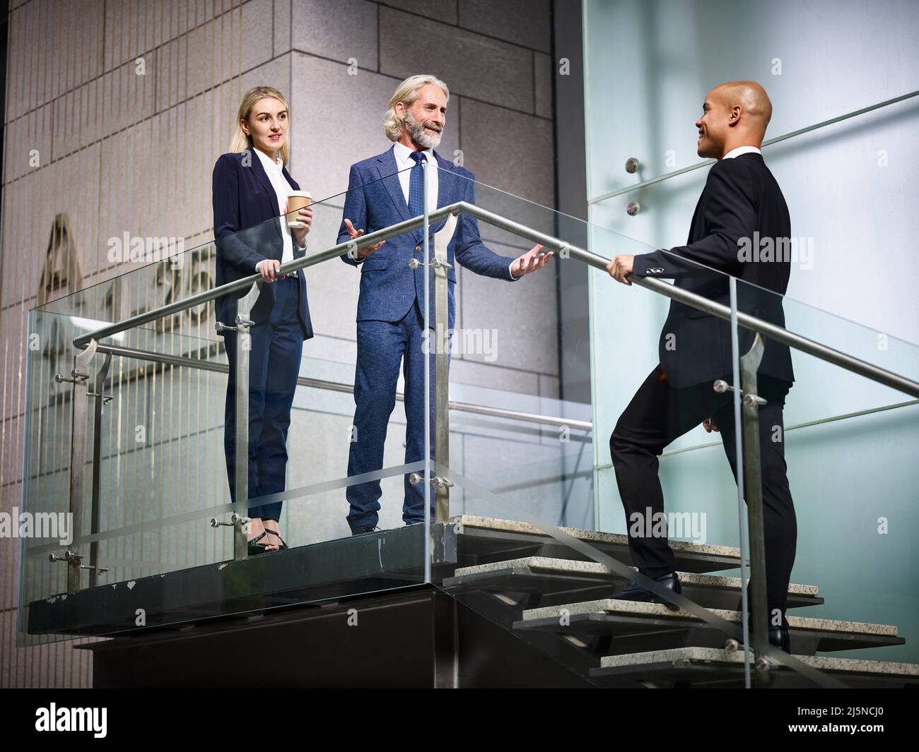 caucasian businessman and businesswoman welcoming latino client inside of modern office building Stock Photo