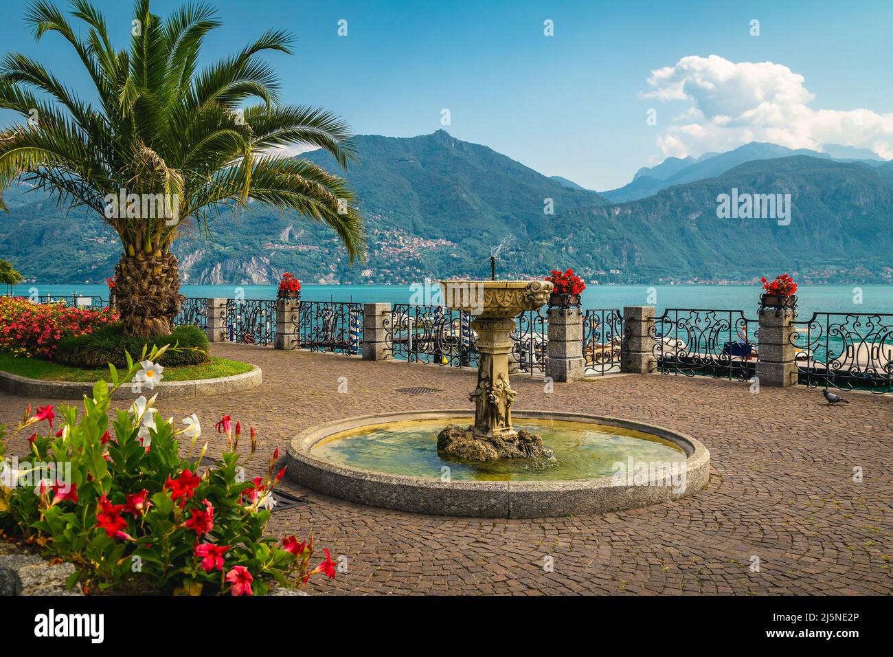 Cute small water fountain and flower decoration with palm trees on the promenade. Fantastic location with view on the shore of the lake Como, Menaggio Stock Photo