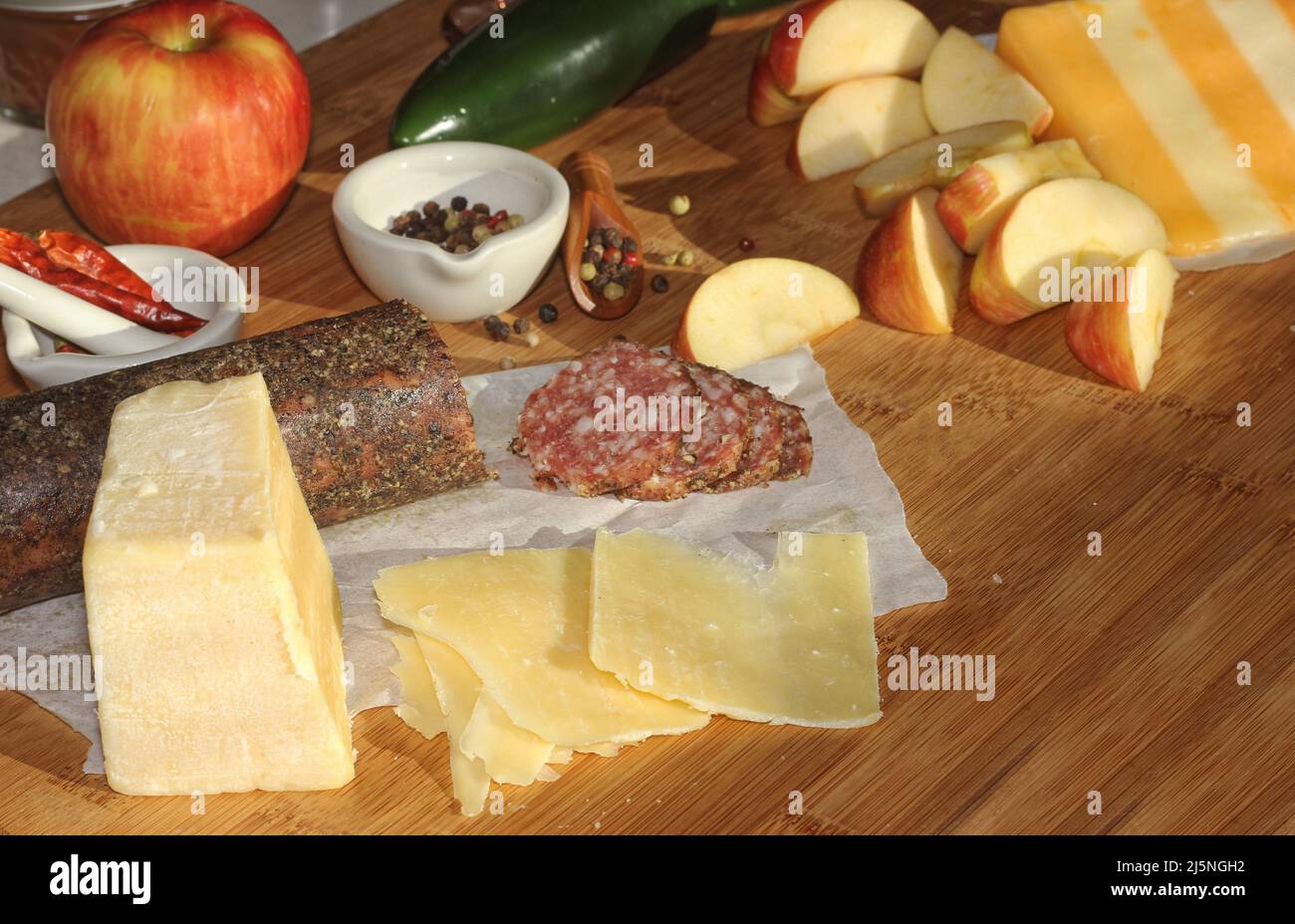 Peppercorn Salami on Tray With English and Irish Cheese, Sliced Apples and Spices in Rustic Kitchen With Light Coming Through Kitchen Window Stock Photo