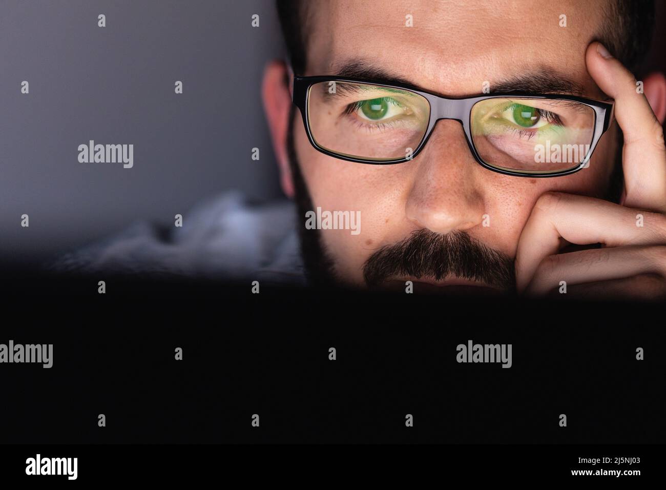 Close up of young adult man in glasses working on laptop computer at night Stock Photo