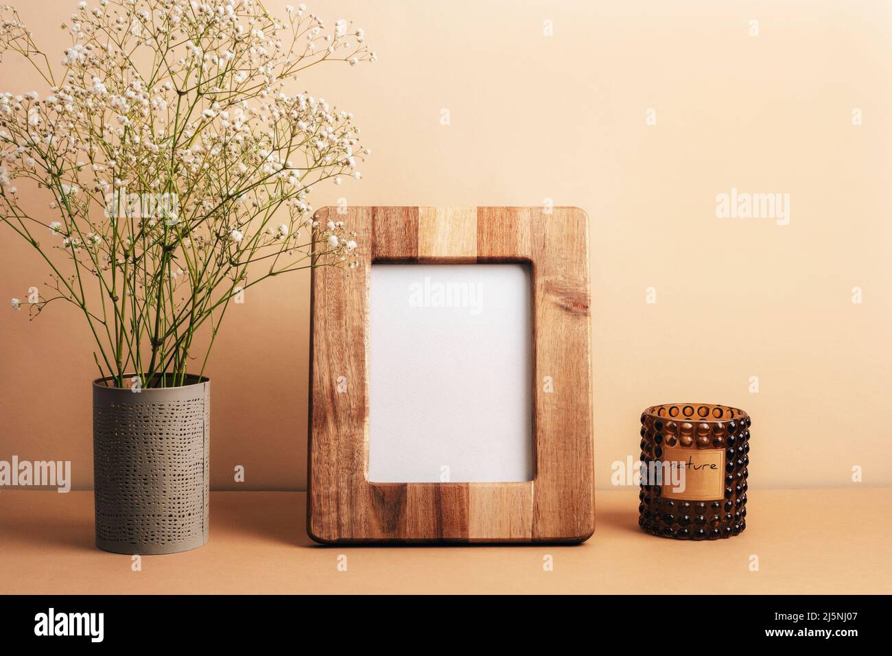 Blank picture frame, aroma candle and gypsophila flowers in vase on ...