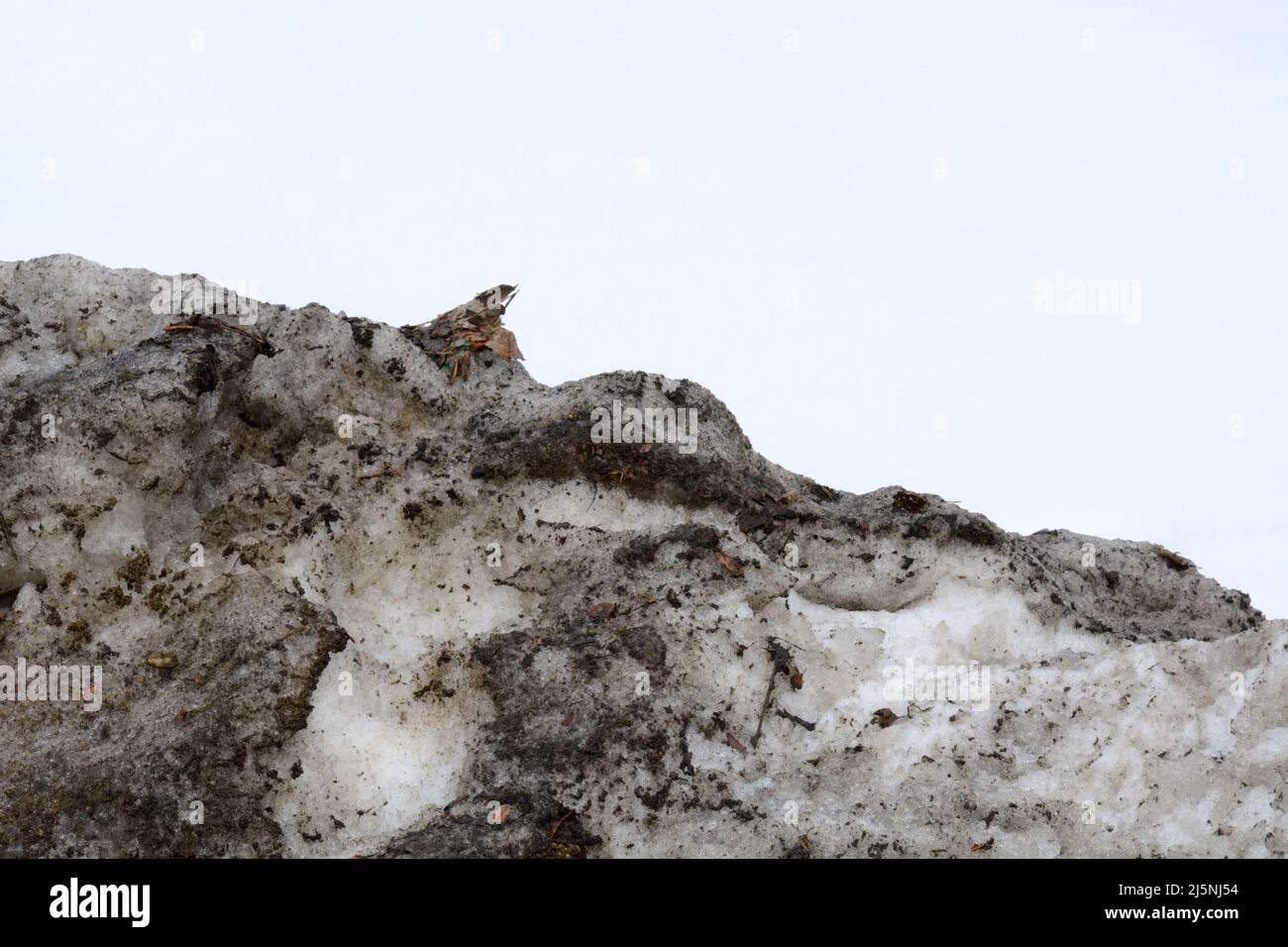 Old pile of dirty snow against white snowy sky Stock Photo