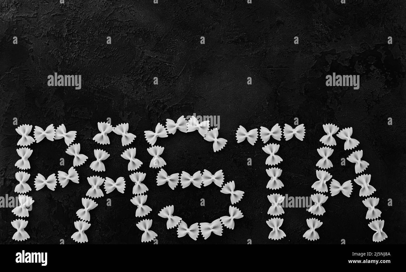 The word pasta written with raw farfalle. Italian is a type of pasta