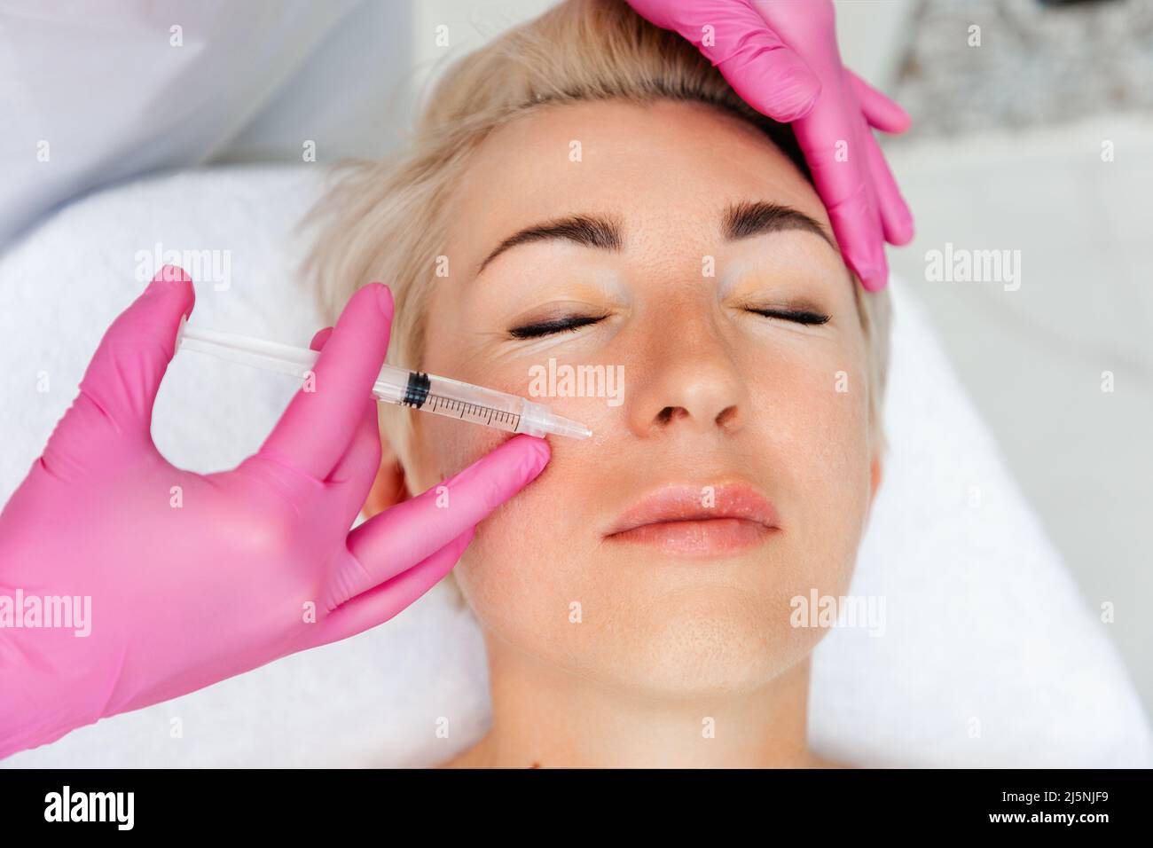 Professional cosmetology. Close-up portrait of beautiful adult woman getting injection in the cosmetology salon. Doctor in medical gloves with syringe Stock Photo