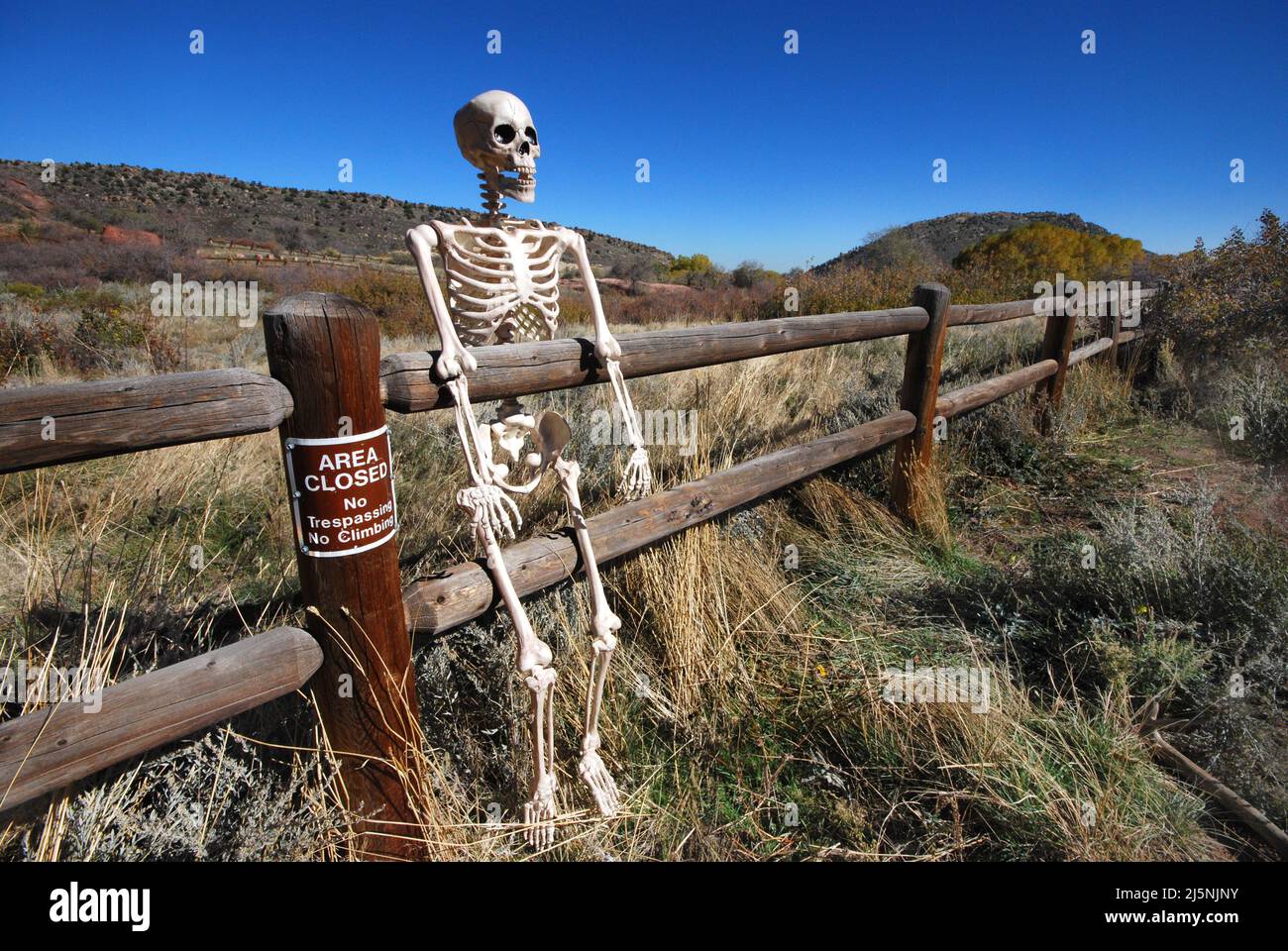 Skeleton resting on wooden pole rail fence in area closed to hikers next to no trespassers no climbing sign Stock Photo