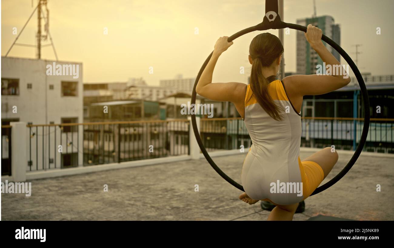 Woman in sportswear doing sky yoga on the rooftop in the evening when the sun set. Self care and health concepts. Stock Photo