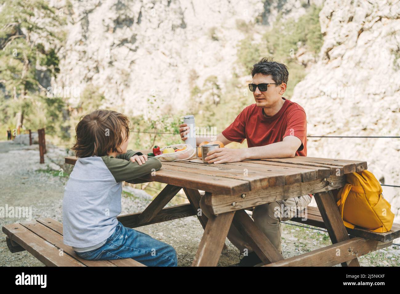 Close-up view of father and his school boy son on a family picnic in the mountains. Child kid and his dad taking a rest and enjoying a picnic while Stock Photo
