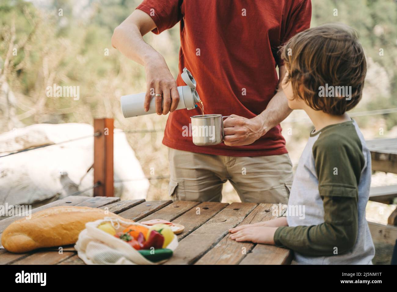 https://c8.alamy.com/comp/2J5NM1T/father-dad-pours-hot-coffee-tea-from-thermos-into-the-mug-on-a-family-picnic-in-the-mountains-child-school-boy-kid-is-watching-his-dad-filling-the-2J5NM1T.jpg