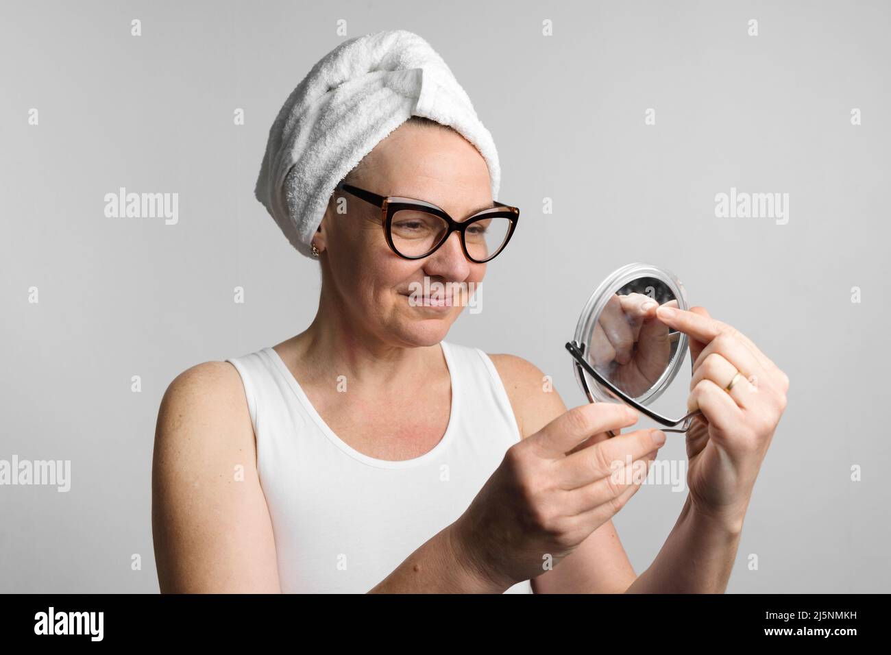 Middle age caucasian woman after bath looking in her mirror reflection. Daily routine of facial treatment  Stock Photo
