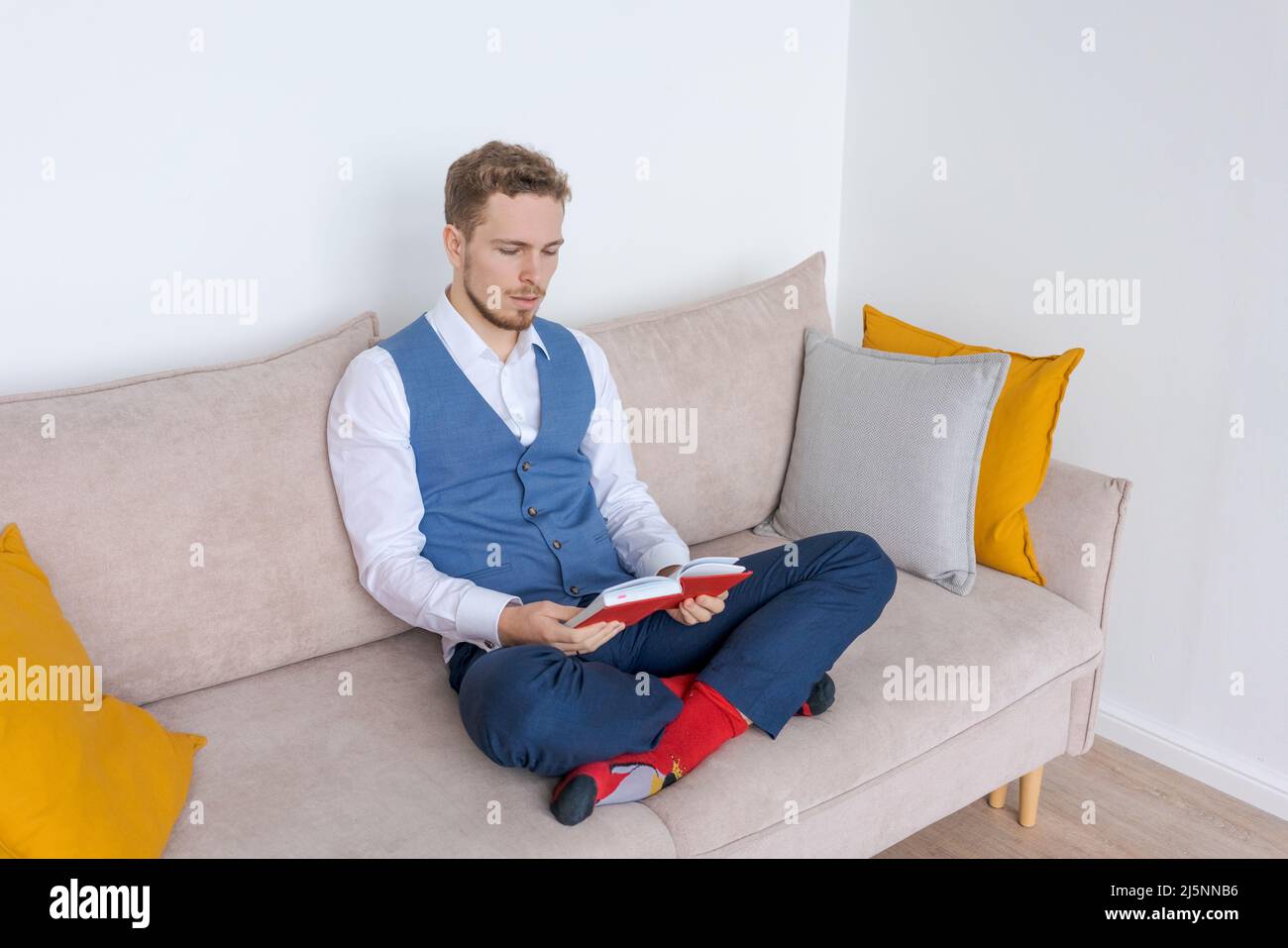 Successful young business man sits on sofa in lotus position in blue suit with notepad and thinks about business plans. Caucasian businessman meditates in the office on the couch Stock Photo