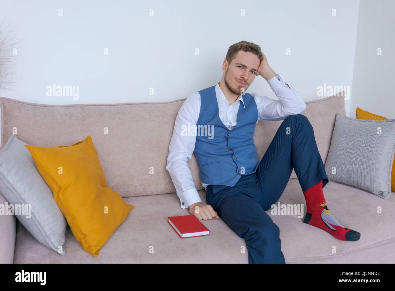 Pensive businessman sits on sofa with diary in his hand, thinks about plans in a blue bearded guy suit. Plans his daily routine and business meetings. Record keeping and planning concept Stock Photo