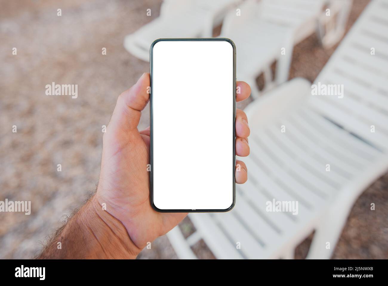 Mobile smart phone with blank mockup template screen in male hand, deck chair lounger in background, selective focus Stock Photo