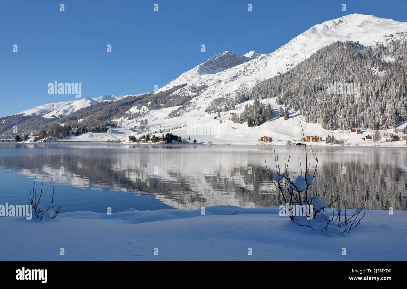 Panoramic view of beautiful white winter wonderland scenery in the Alps with snowy mountain summits reflecting in crystal clear mountain lake on a col Stock Photo