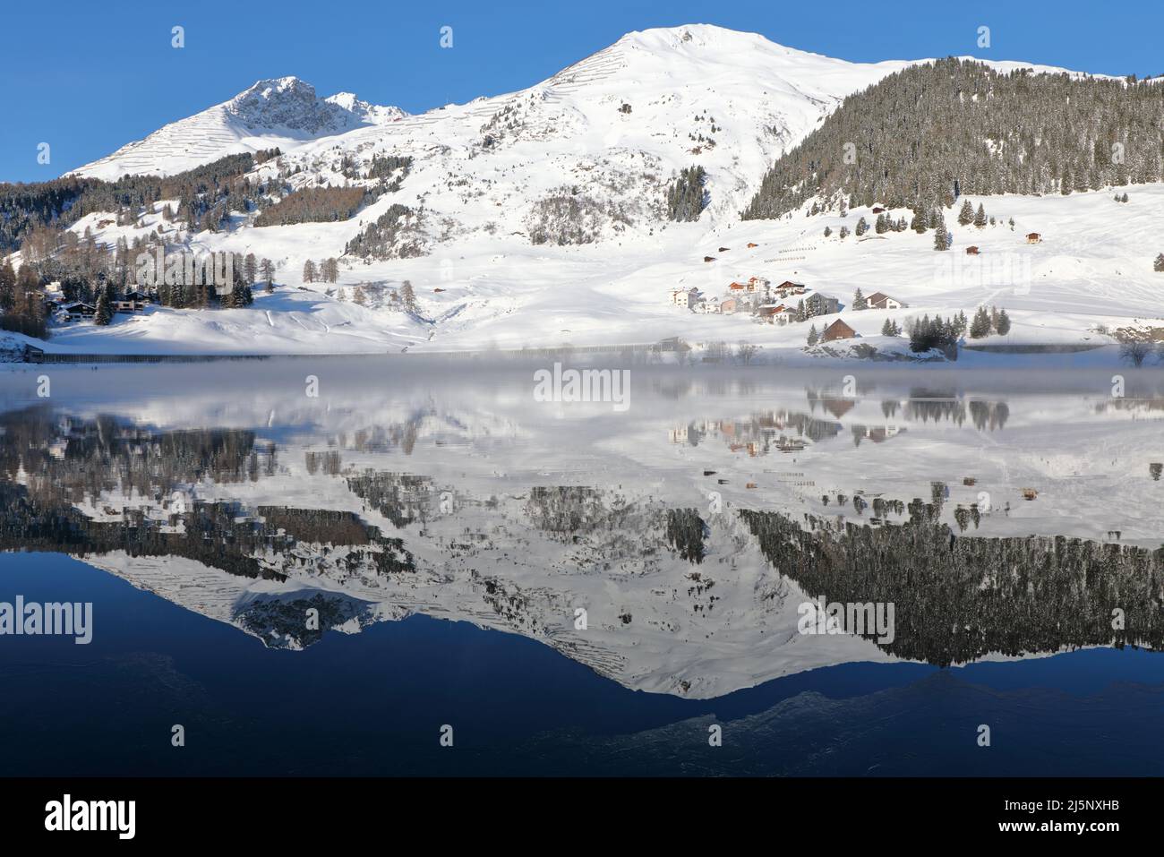 Panoramic view of beautiful white winter wonderland scenery in the Alps with snowy mountain summits reflecting in crystal clear mountain lake on a col Stock Photo