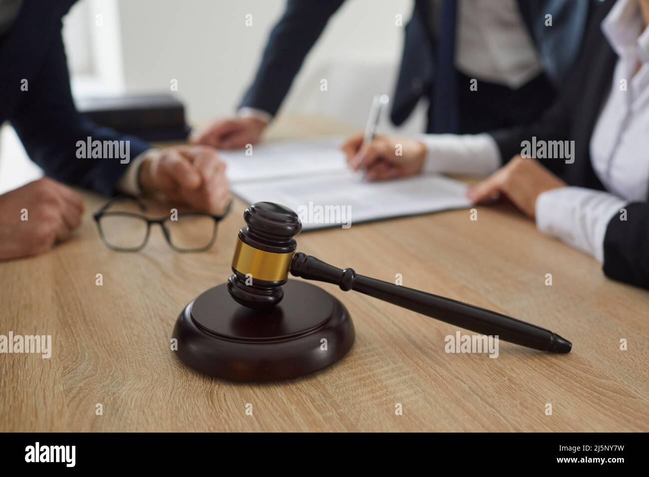 Judge's gavel on a wooden table, and a lawyer giving legal advice to clients in the background Stock Photo