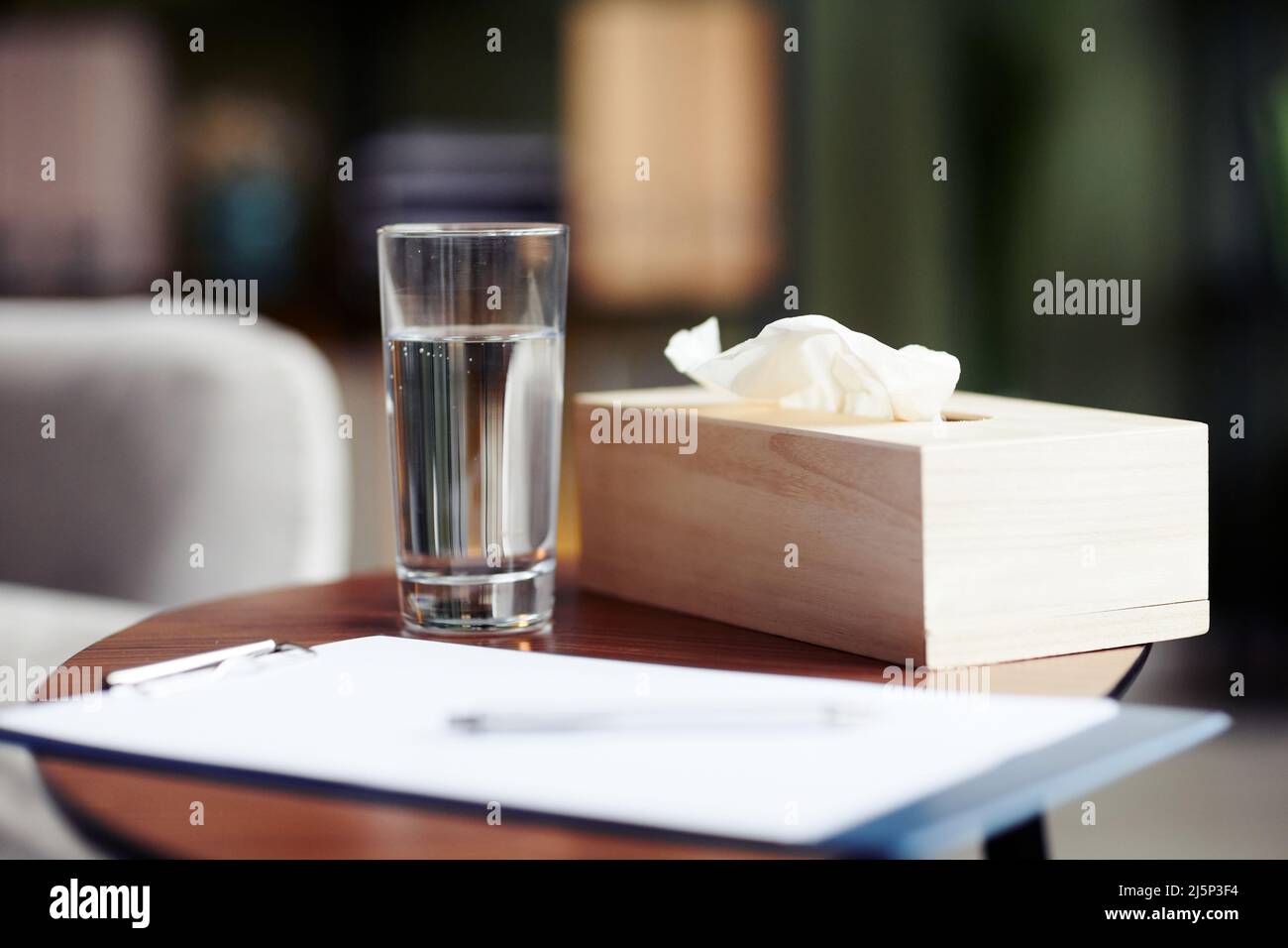 Glass of fresh water, blank sheet on clipboard and napkins for client on table in office of therapist Stock Photo