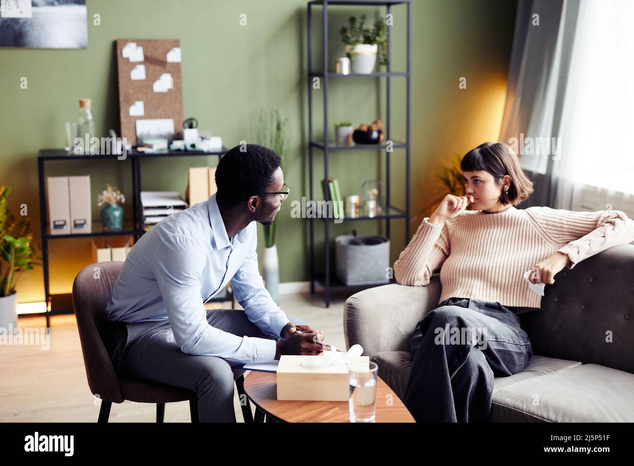 Psychologist talking to young woman in private therapy session Stock