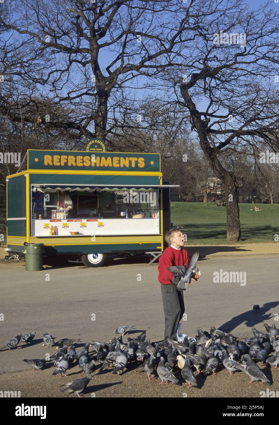 young boy feeding doves and a soft drink kiosk in Hyde Park London, England Stock Photo