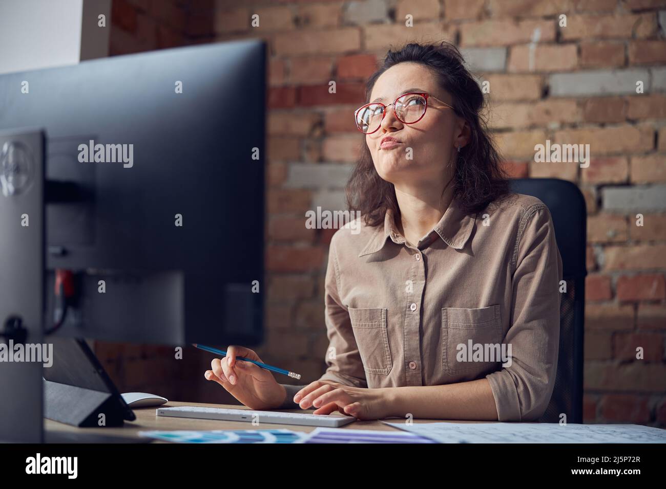 Thoughtful female interior architect or designer working on a project, using computer while sitting at the desk in her office Stock Photo