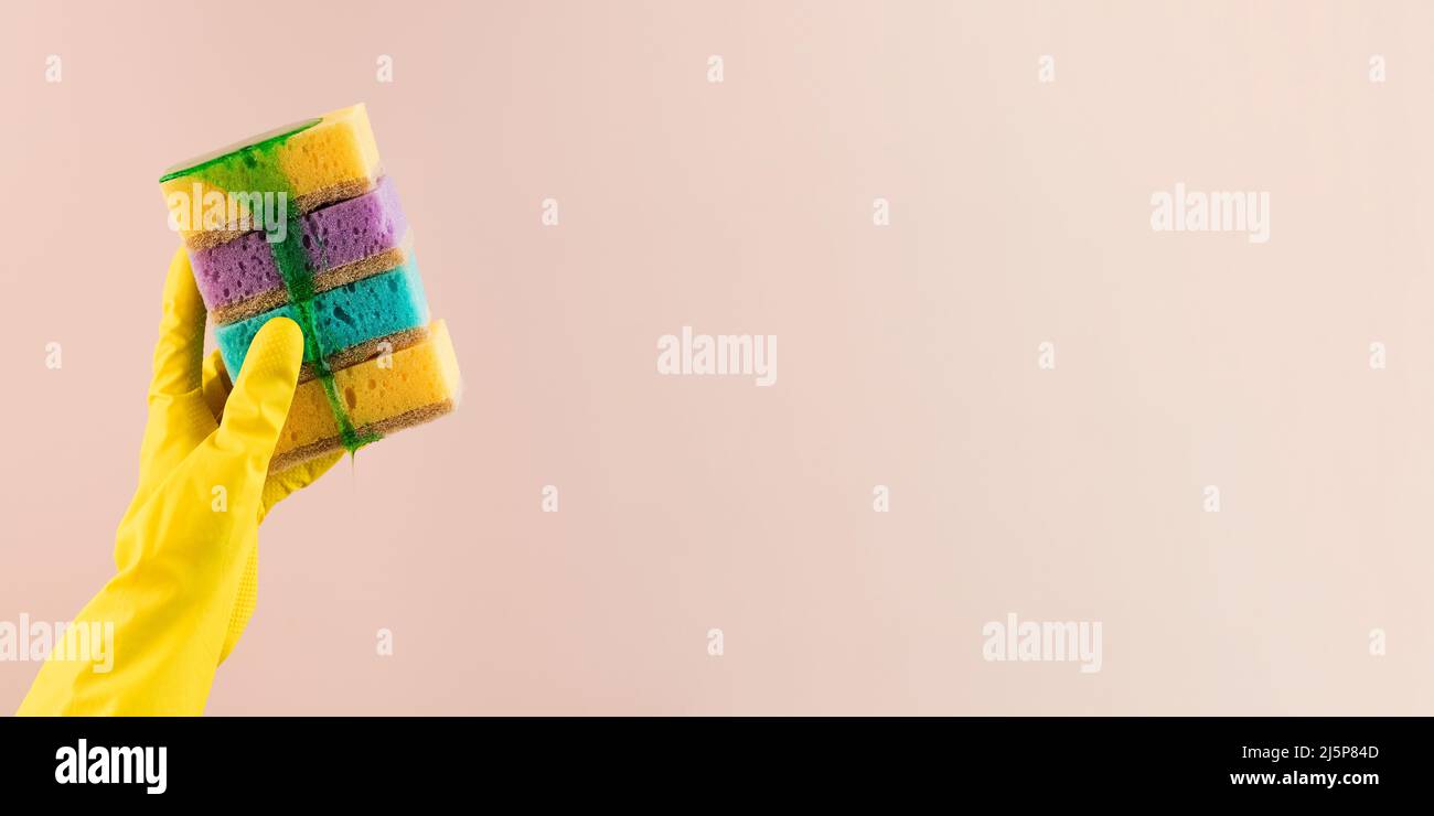 A hand in a yellow rubber glove holds colorful sponges for dishes from ...