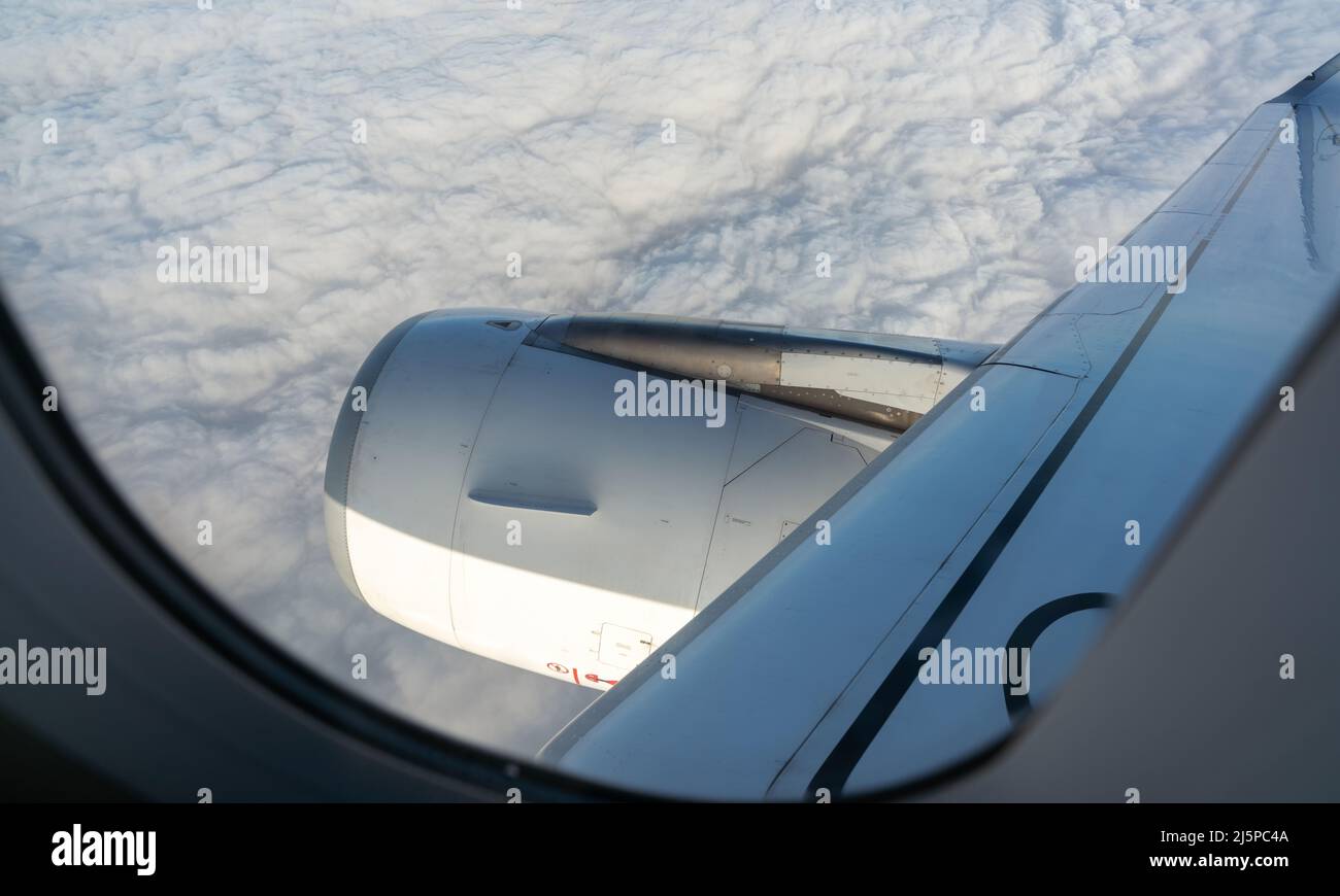 View from inside plane through a plane window over white clouds. Window view of the plane sees an airplane engine. Airplane flying in the sky. Stock Photo