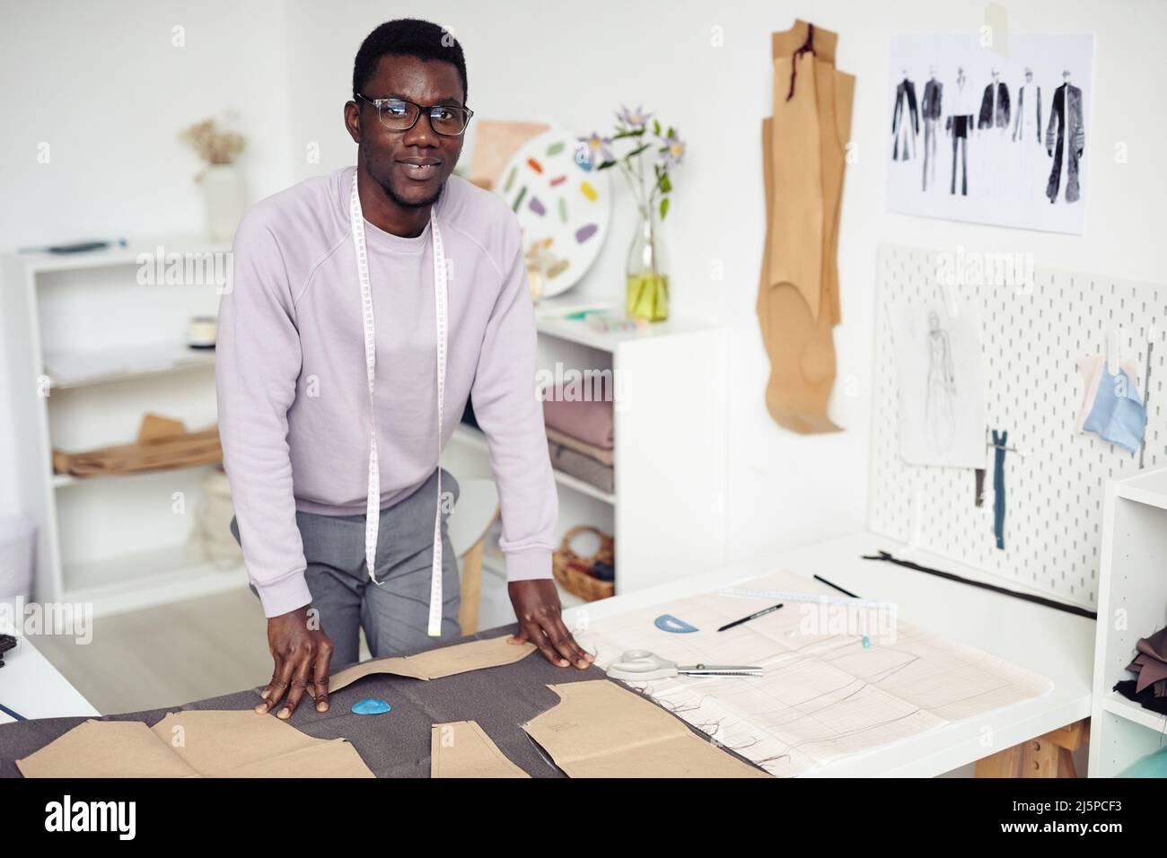 Portrait of young smiling African American tailor leaning on table with ...