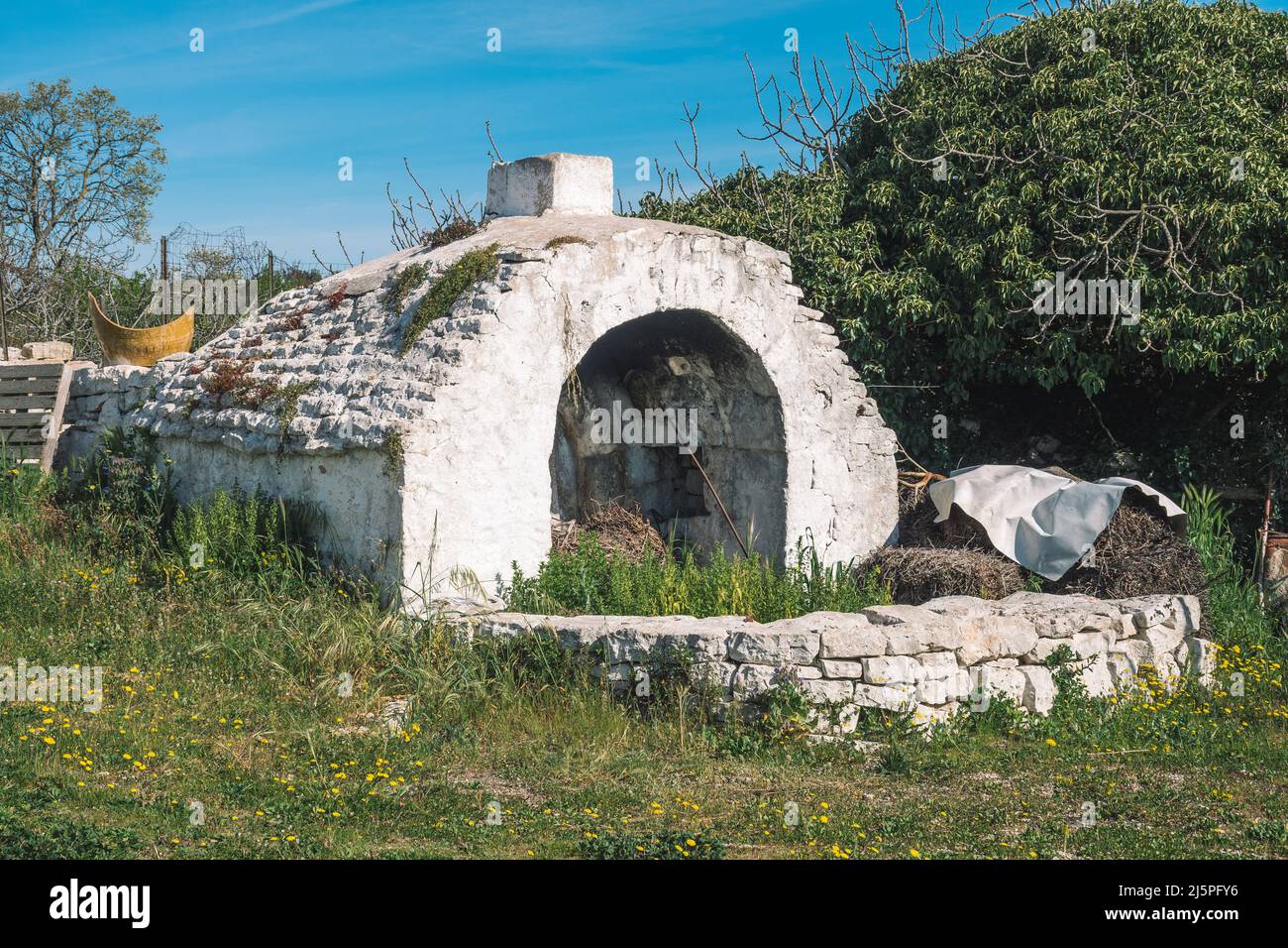 Beautiful white traditional old stone outdoor oven or fireplace in the countryside in Puglia region, Italy with dry stone wall and nature around Stock Photo