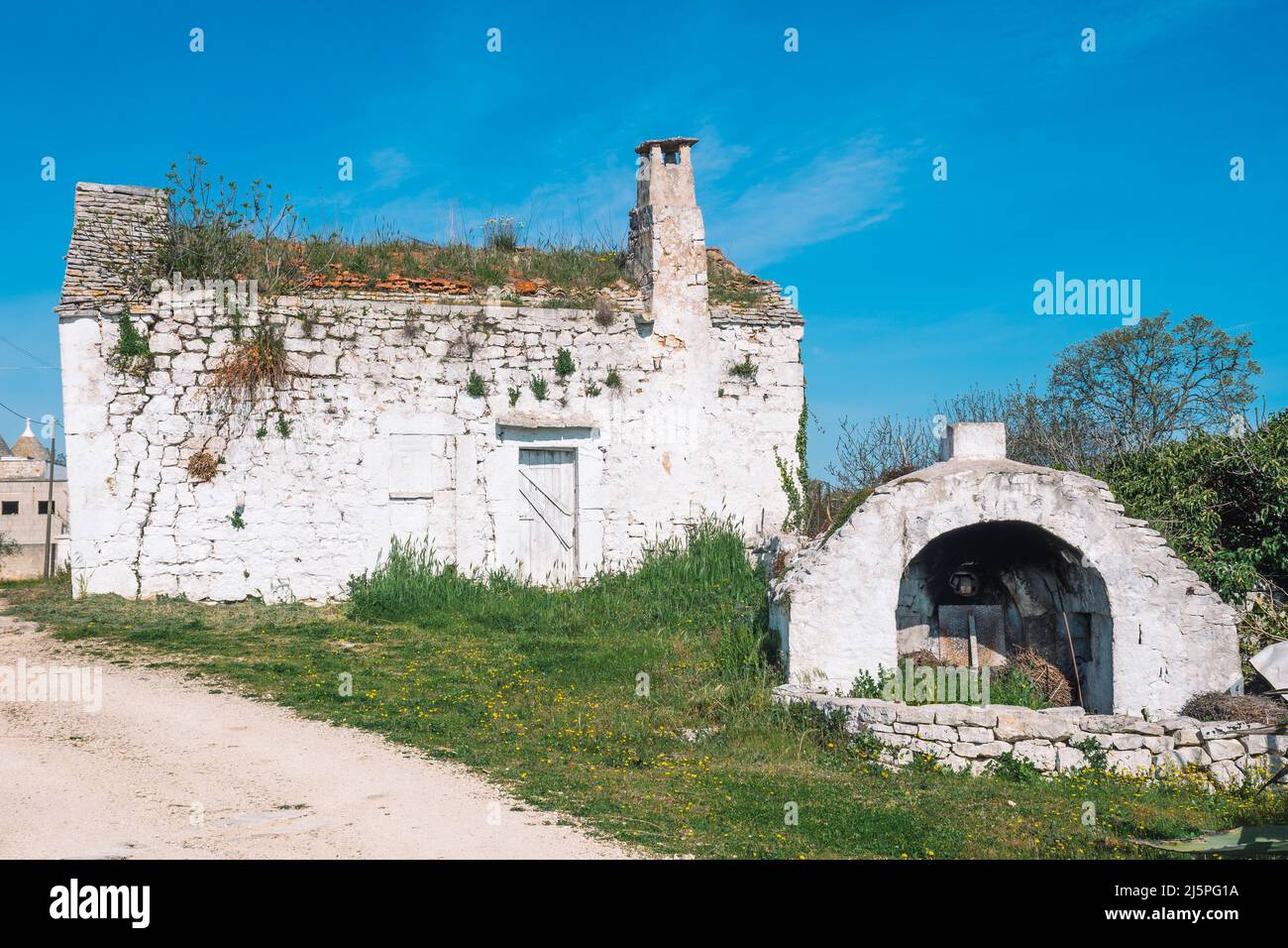 Beautiful white traditional old stone outdoor oven or fireplace in the countryside in Puglia region, Italy with dry stone wall and nature around Stock Photo