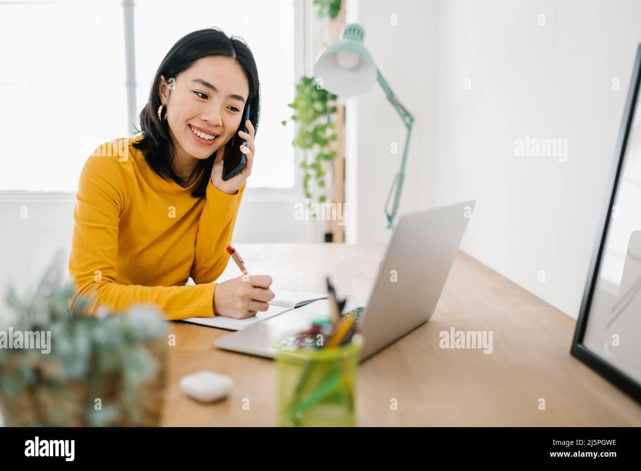 Woman talking on her mobile phone while working with a laptop computer at home. Stock Photo