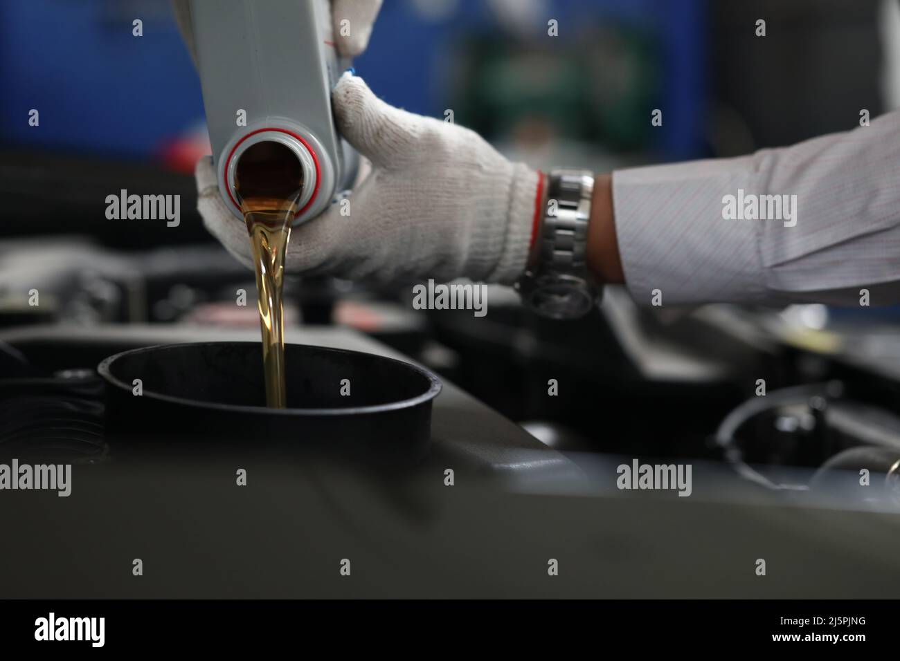Auto mechanic refueling and pouring oil into engine motor ia car Stock
